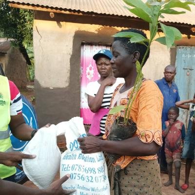 A lady holds a seedling and a sack of food that she has just received